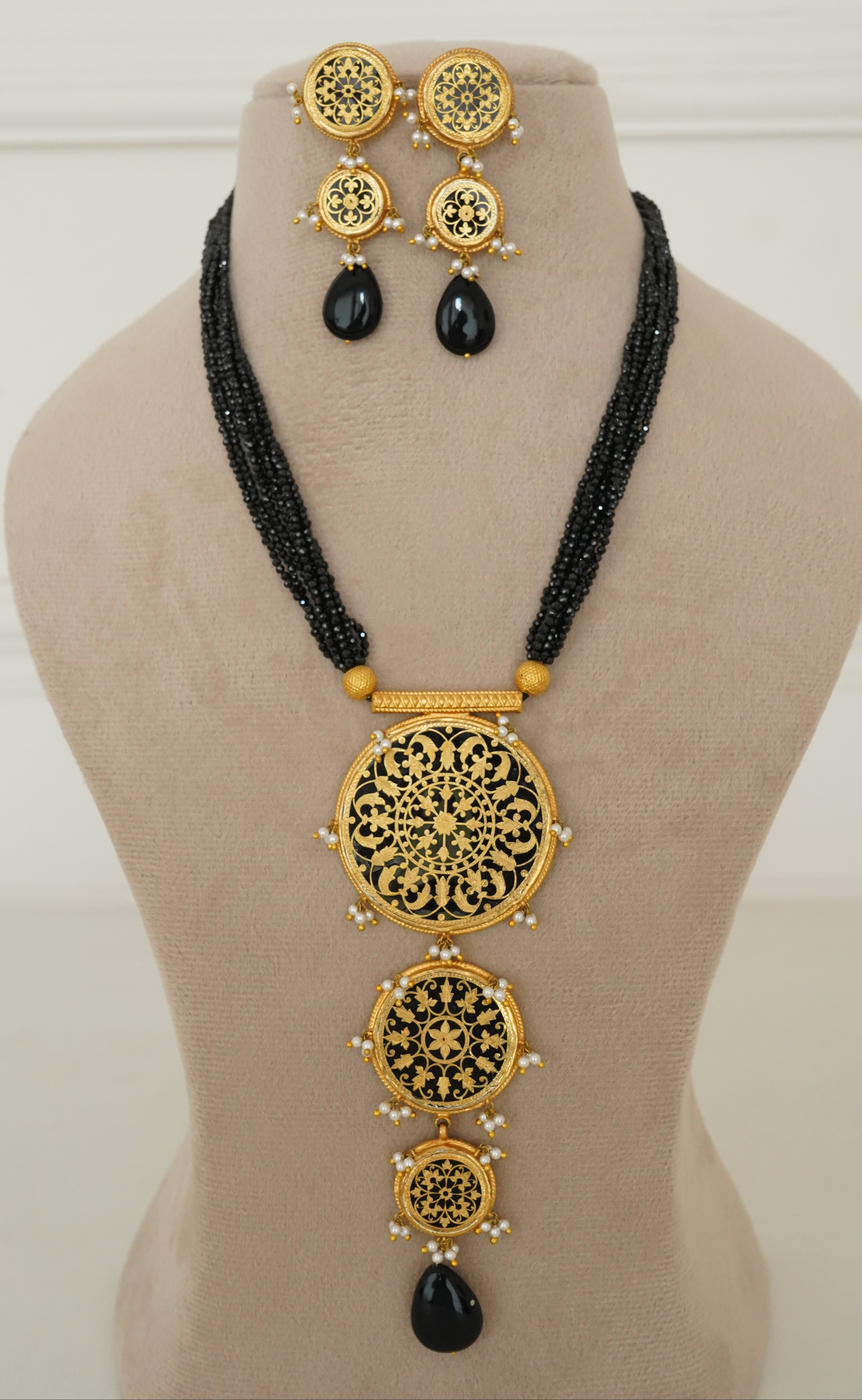 Gold and black traditional Indian jewelry set displayed on a beige mannequin bust, including a necklace, earrings, and a waist chain with ornate filigree circular designs.