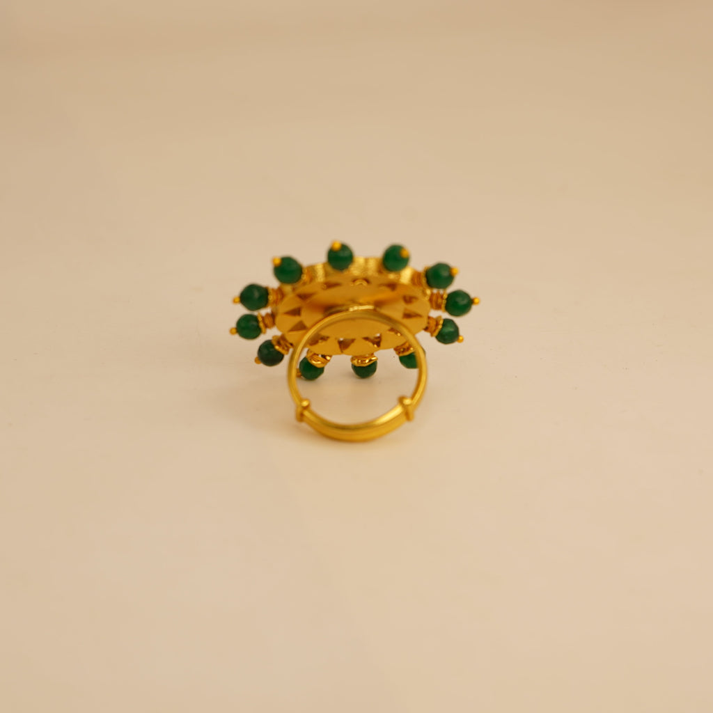 Gold ring with green gemstones on a beige background