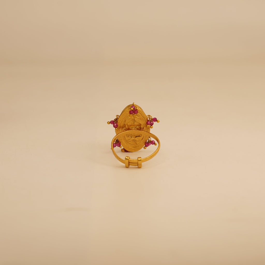 Gold ring with red gemstones on a beige surface