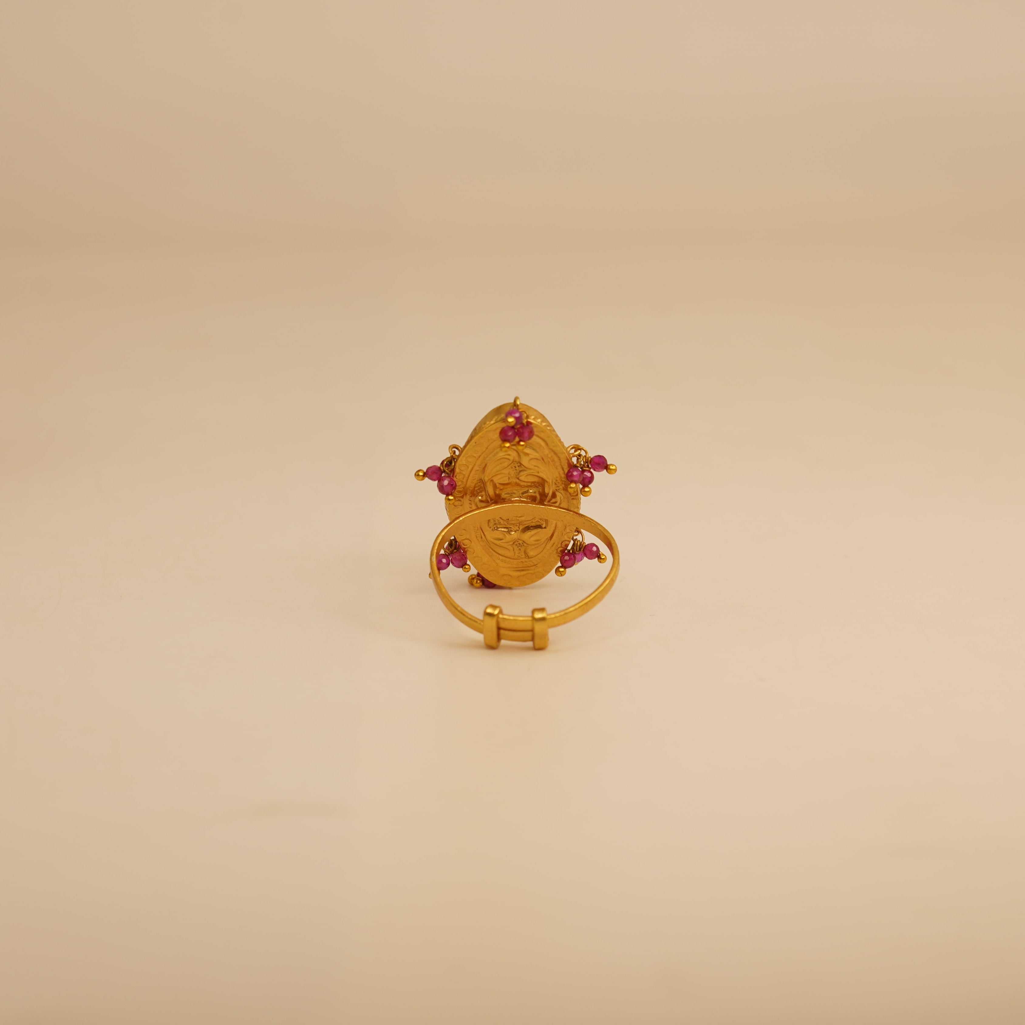Gold ring with red gemstones on a beige surface