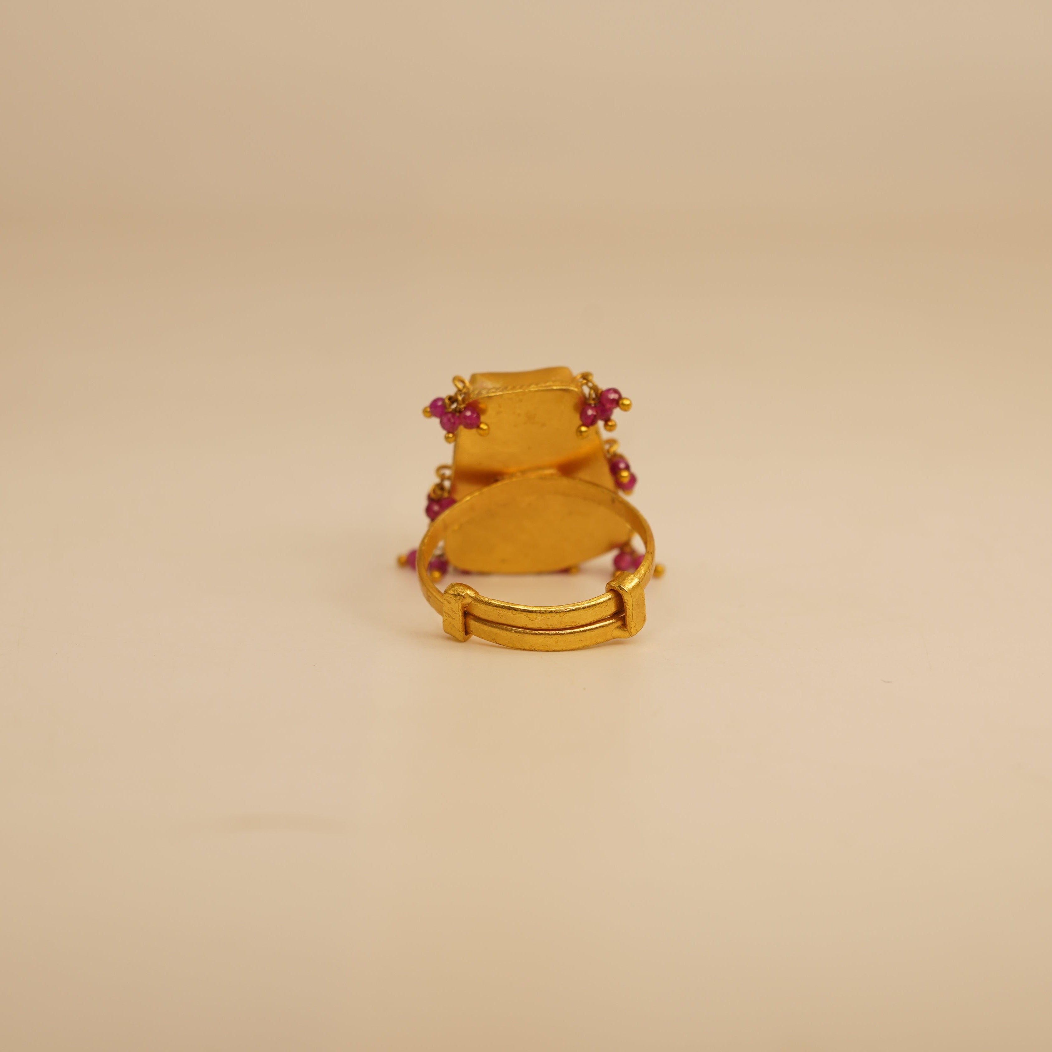 Gold ring with red gemstones on a beige background