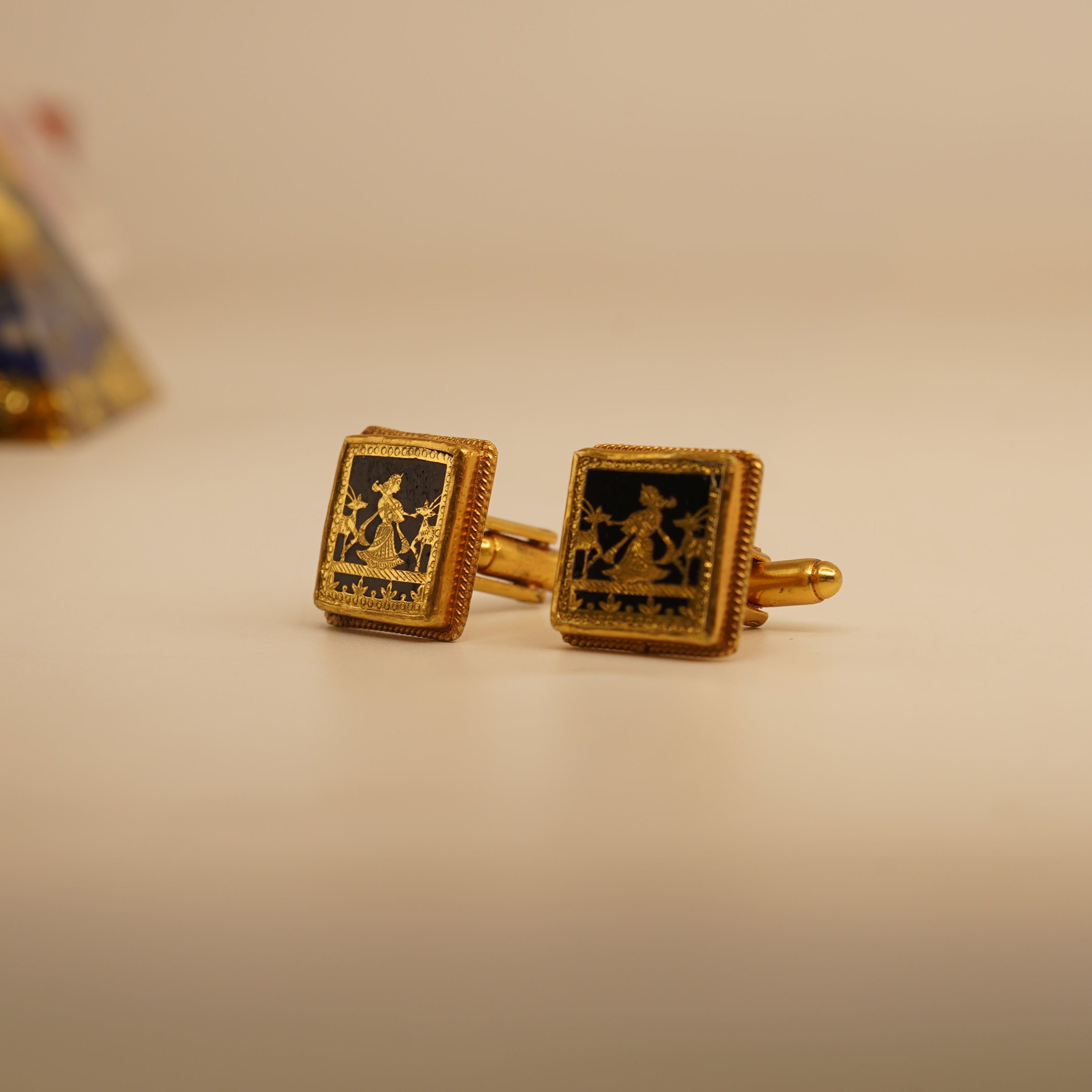 Gold cufflinks with intricate design on a beige background